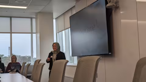 Doctoral student presents in front of a large video screen.