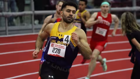 A man runs on a track wearing a yellow and purple jersey with the number 4 and UAlbany written on it.