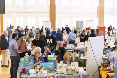 A large group of people mingle amid rows of books on tables indoors.