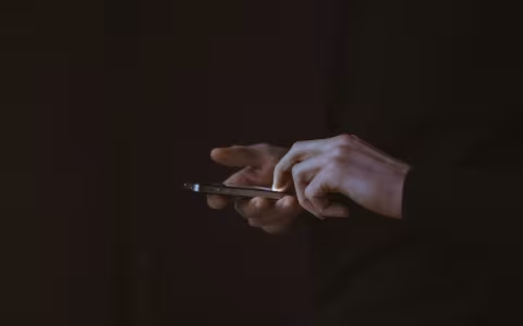 hands using a cell phone against a dark background