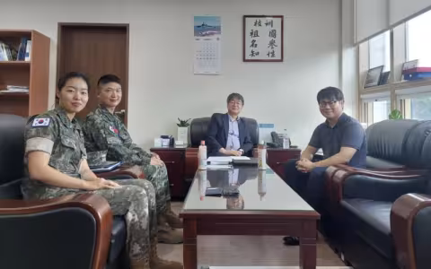 Two people in militaty fatigues and two in civilian clothing sit around a glass-topped table.