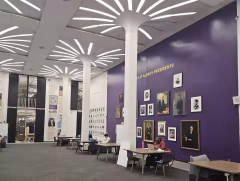 Students study at individual study tables in front of the a wall with paintings of UAlbany Presidents inside the University Library.