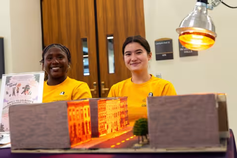 Two students sit behind a 3D model of a city landscape.