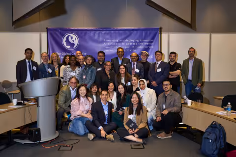 About 30 people pose for a photo in front of a GCAIMH Annual Summit banner.