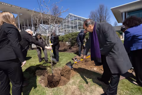 President Rodriguez shovels dirt to help plant a tree in front of the UAlbany greenhouse.