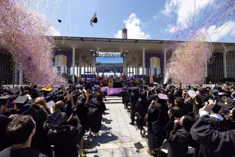 Students in regalia throwing their caps and celebrating at Commencement.