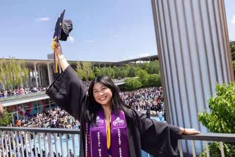 Student holding her mortarboard up in celebration in front of the fountain.