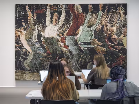 Students working on laptops in front of tapestry work