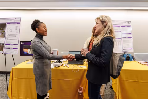 Two women smile and shake hands in front of a table