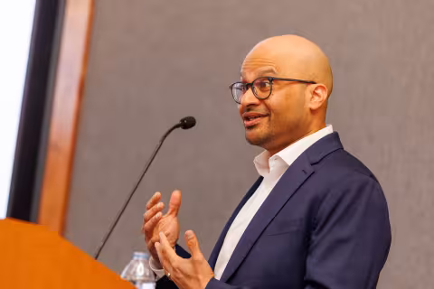 A man wearing glasses gestures as he speaks into a microphone