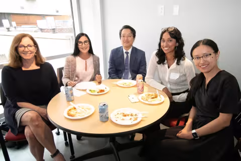 Five individuals sitting at a table with food smiling at the 2nd Annual Summit for the Global Center in AI Mental Health at the Suny Global Center in NYC.