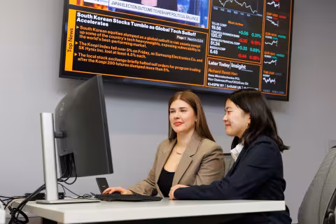Two young women sit at a Bloomberg terminal inside of the UASBIG suite at UAlbany's Massry School of Business