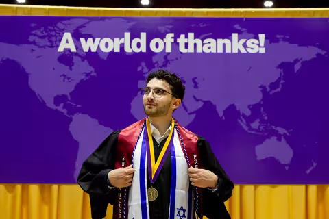 Student in regalia posing in front of a sign that says A world of thanks!