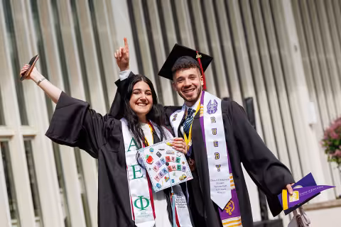 Two students in full regalia posing with their arms in the air.