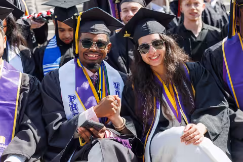 Two students in full regalia holding hands and smiling at Commencement.