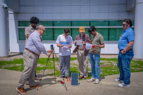 People gather around a solar panel for a workshop on energy storage technologies