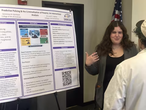 One individual stands next to a project poster talking to another individual.
