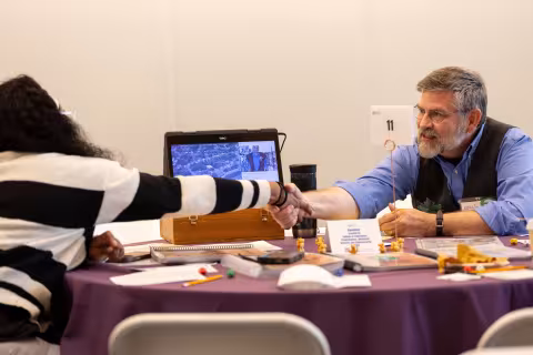 A researcher and a student seated at a table shake hands during a RISE pitch session.