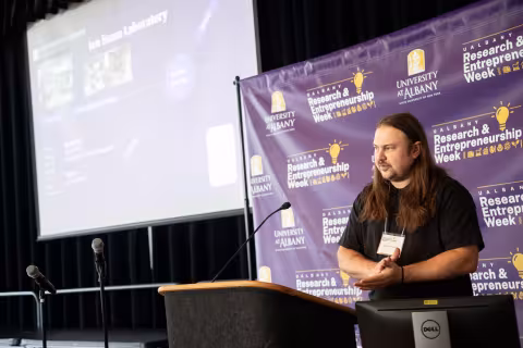 A researcher stands at a podium and speaks about the Ion Beam Laboratory during R&E Week 2023.