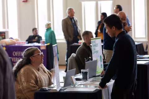 An R&E Week 2023 attendee stops to speak with a University employee staffing a table with information about entrepreneurship.