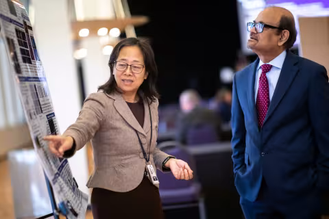 A faculty member points to her research poster while conversing with UAlbany Vice President for Research & Economic Development Thenkurussi (Kesh) Kesavadas.