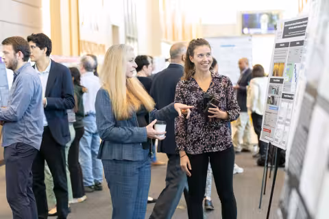 A researcher smiles as she speaks with an R&E Week attendee, who is gesturing toward her research poster.