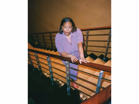 Artist Salome Asega on a stairwell looking up at the camera
