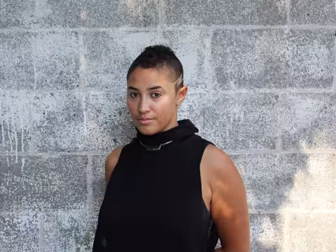 Scholar Kali Tambree in front of a cinderblock wall