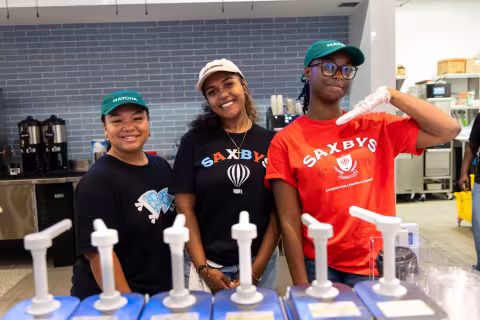 Three students stand behind flavor shot bottles inside a new Saxbys cafe within UAlbany's Massry School of Business