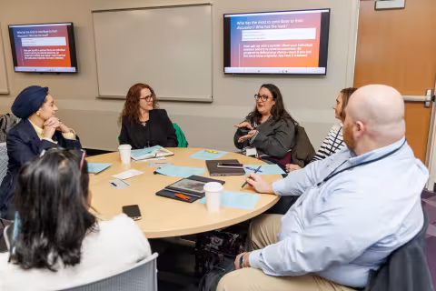 Six people sit at a round table having an in-depth discussion during the 2026 AI Plus Symposium.