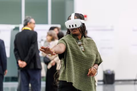 A person wearing a virtual reality headset reaches out their hand during the 2026 AI Plus Symposium.