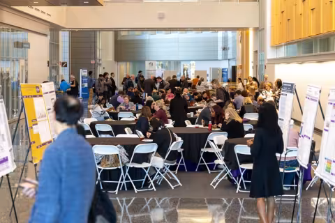 A large crowd of people seated at circular tables in a open building atrium.