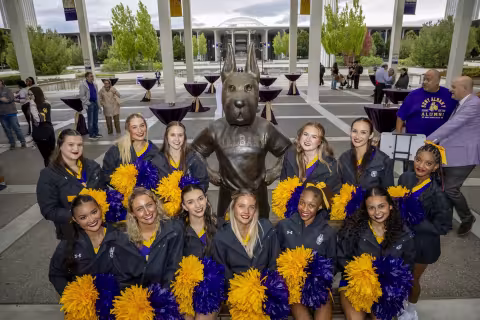 The UAlbany cheer team takes a photo with the Damien statue.