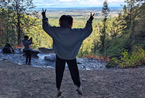 A student jumps and holds up two peace signs while hiking an upstate trail.