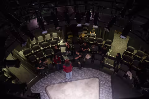 A photo taken above a theatre-in-the-round at UAlbany's Performing Arts Center looking down as students prepare for a performance.