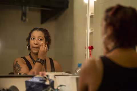 A student applies makeup while preparing for a performance as they look in a mirror