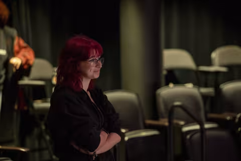 A woman with pink hair watches off stage during a theatre production indoors at UAlbany
