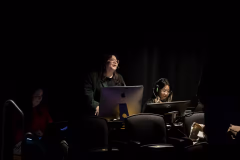 Two stage crew members listen and watch a darkened stage during a performance at UAlbany's Performing Arts Center
