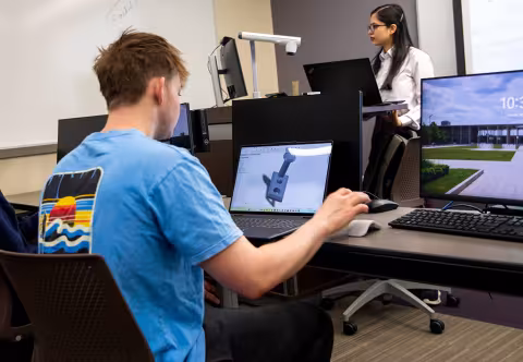 A student listens to a professor in class in the MME program while they use a computer.