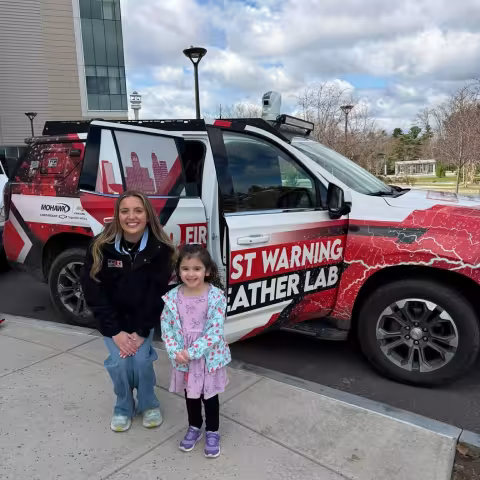 A child stands with WNYT meteorologist Alexa Dringus in front of the the First Warning Weather Lab.