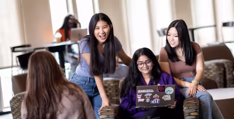 Four students smile and laugh as they hang out in a group study area.