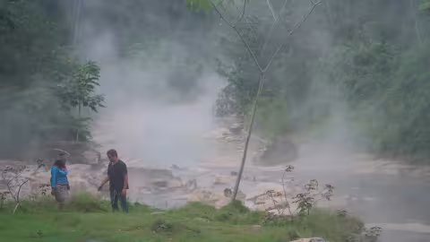 A man and woman stand near a steaming river deep in the jungle