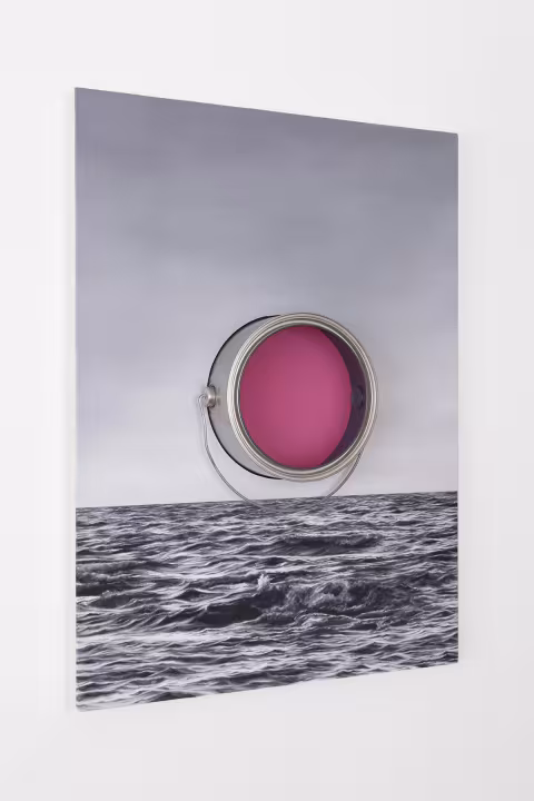 An oil painting of a gray ocean and sky hung on a wall, with a paint can protruding from the center. Inserted inside the paint can, is a circle of pink, translucent glass. 