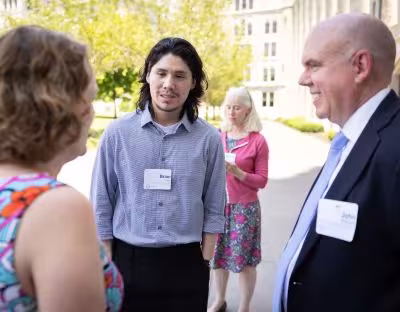 A young man in a blue shirt and nametag reading Brian, stands between a man and a woman, both partially visible.