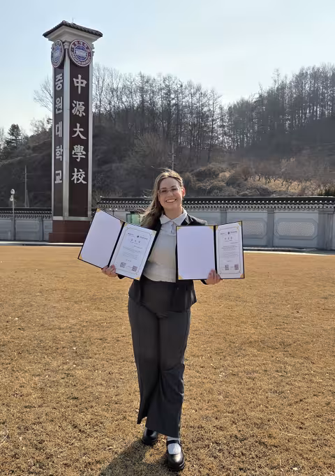 Kate Bucek stands in Korea with her awards from Fulbright for learning the Jeju dialect of Korean.