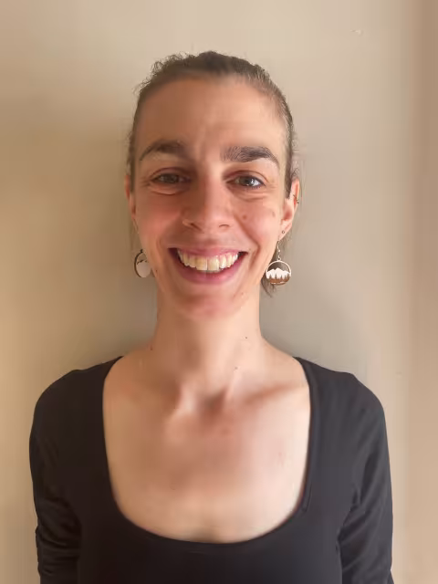 A young woman wearing a black top smiles for a portrait against a beige wall. 