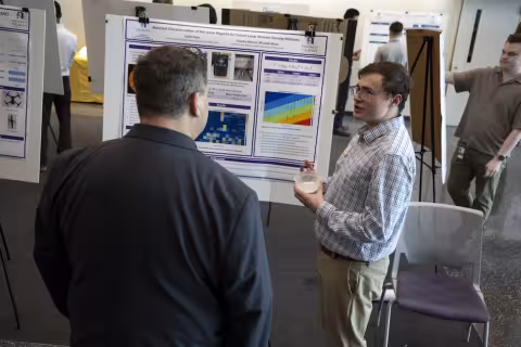 A young man talks to another man in front of a research poster