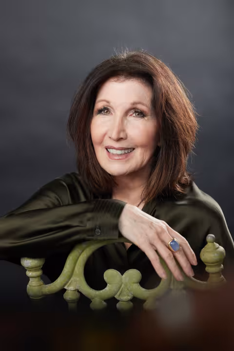 woman with dark hair smiles as arm is draped over the back of a chair