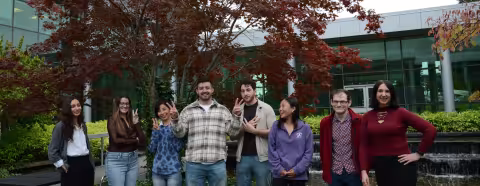 Research Scientist Megumi Akamatsu and seven student researchers laugh as they pose for a silly photo outdoors.