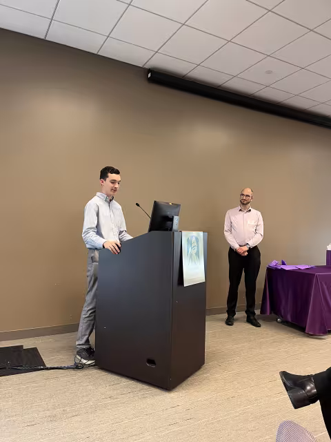 Political science student Trevor Pettit stands at the podium to give remarks about his professor Brian Greenhill, standing to the right of him..